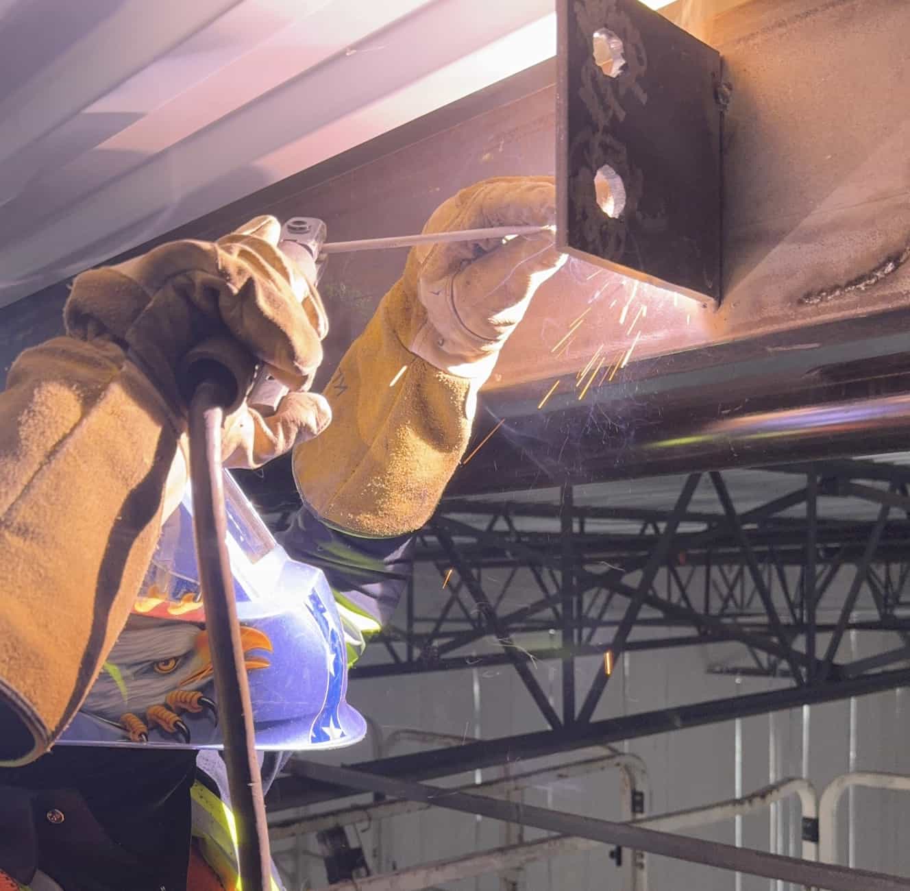 Close-up of stick welding a structural connection bracket onto a steel beam