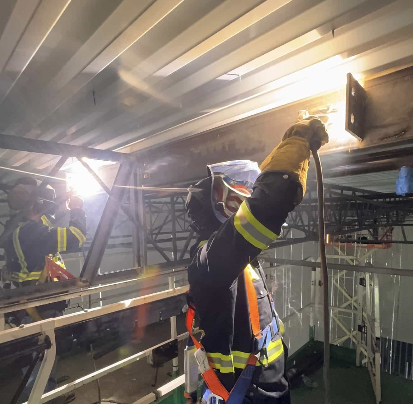 Soldadura en altura sobre acero estructural con el equipo trabajando al lado